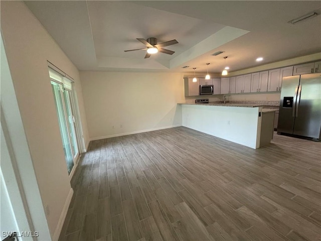 kitchen with decorative light fixtures, a raised ceiling, wood-type flooring, kitchen peninsula, and stainless steel appliances