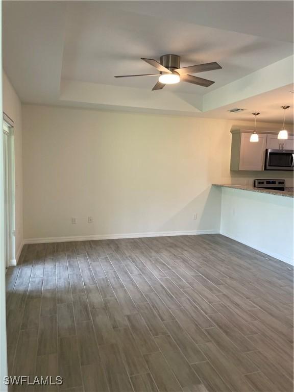 unfurnished living room featuring dark wood-type flooring, a raised ceiling, and ceiling fan