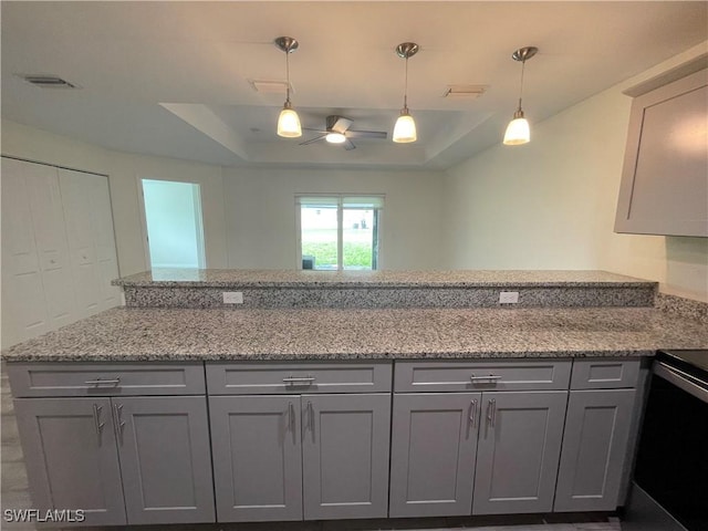 kitchen featuring gray cabinetry, a tray ceiling, light stone countertops, and decorative light fixtures