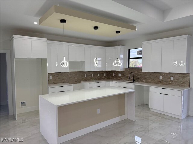 kitchen featuring a center island, decorative backsplash, sink, white cabinetry, and decorative light fixtures