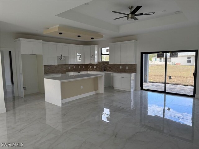 kitchen with tasteful backsplash, white cabinetry, a raised ceiling, and a kitchen island