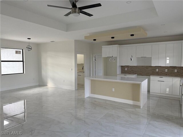 kitchen featuring decorative backsplash, white cabinetry, a tray ceiling, and a center island