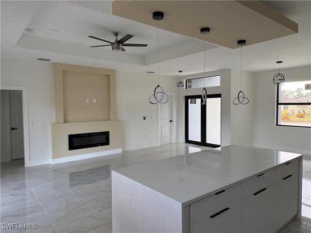 kitchen with ceiling fan, white cabinetry, decorative light fixtures, and a tray ceiling