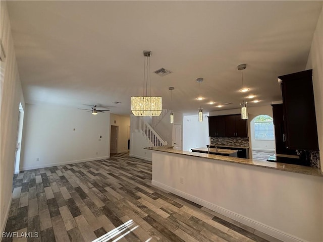 kitchen with hanging light fixtures, ceiling fan, hardwood / wood-style flooring, dark brown cabinets, and tasteful backsplash