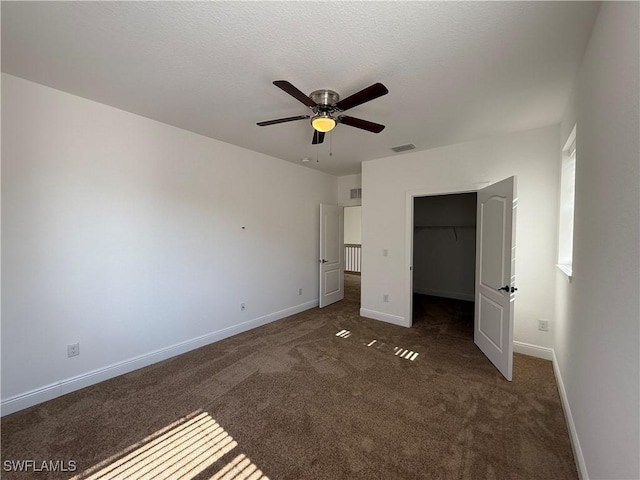 unfurnished bedroom with dark carpet, ceiling fan, a spacious closet, and a closet