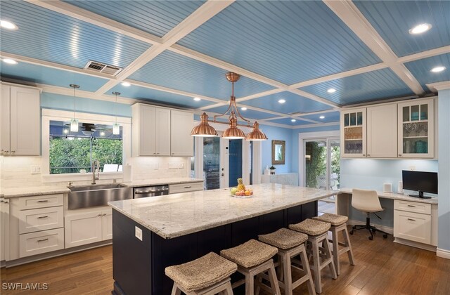 kitchen with sink, white cabinetry, coffered ceiling, a kitchen island, and pendant lighting