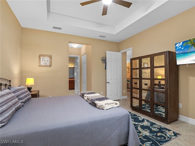 bedroom featuring ceiling fan, light tile patterned floors, connected bathroom, and a tray ceiling