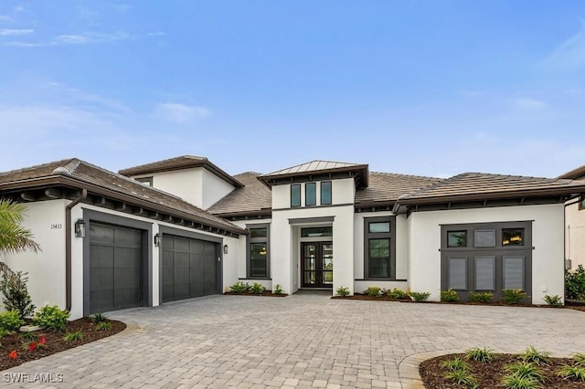 prairie-style house with metal roof, a garage, french doors, decorative driveway, and stucco siding