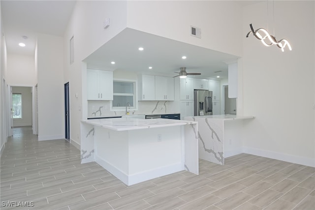 kitchen with a breakfast bar area, kitchen peninsula, pendant lighting, stainless steel refrigerator with ice dispenser, and white cabinets