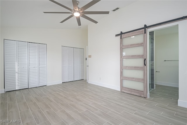 unfurnished bedroom featuring two closets, ceiling fan, vaulted ceiling, and a barn door