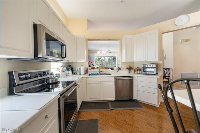 kitchen featuring sink, light hardwood / wood-style flooring, appliances with stainless steel finishes, an inviting chandelier, and white cabinets