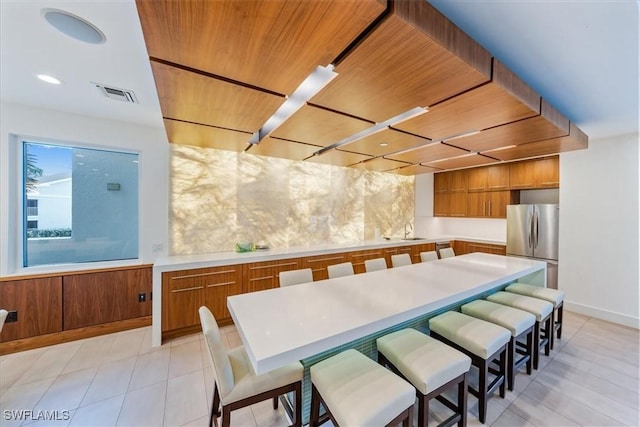 kitchen with stainless steel refrigerator, sink, a breakfast bar area, light tile patterned floors, and wooden ceiling