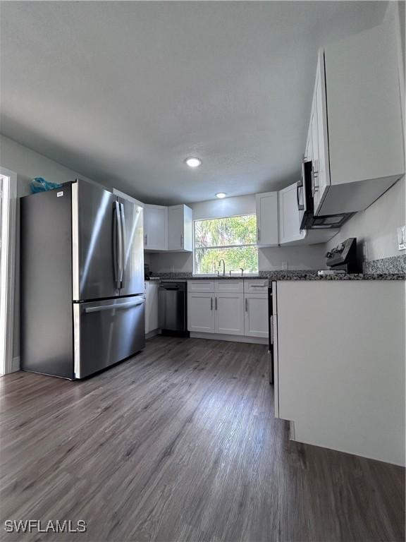 kitchen featuring dark hardwood / wood-style floors, stainless steel refrigerator, white cabinets, dark stone counters, and black dishwasher