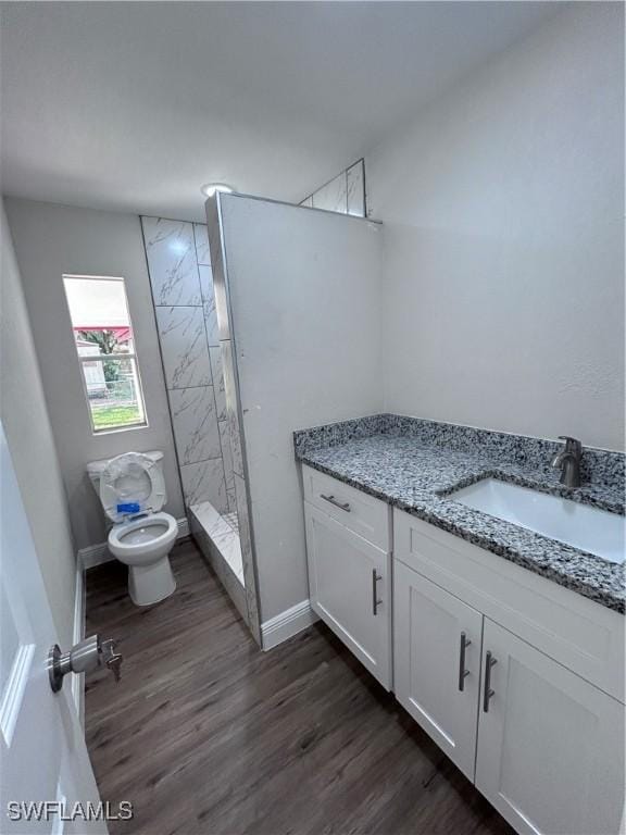 bathroom with toilet, vanity, hardwood / wood-style flooring, and tiled shower