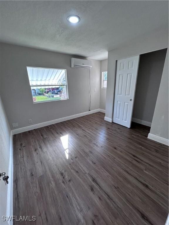 spare room with a wall mounted AC, a wealth of natural light, and dark wood-type flooring