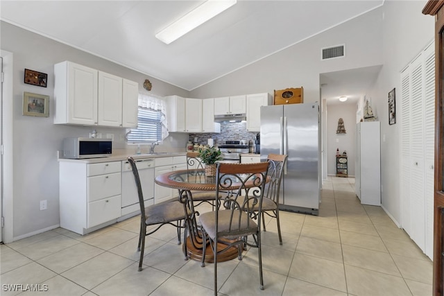 kitchen with tasteful backsplash, vaulted ceiling, light tile patterned floors, appliances with stainless steel finishes, and white cabinets