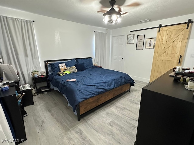 bedroom with ceiling fan, light wood-type flooring, and a barn door