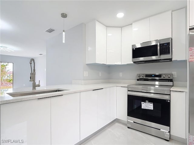 kitchen with appliances with stainless steel finishes, hanging light fixtures, white cabinets, and sink