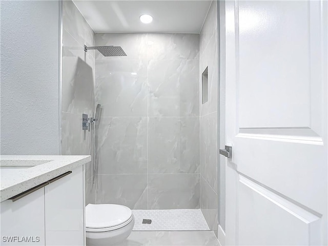 bathroom featuring toilet, tiled shower, and vanity