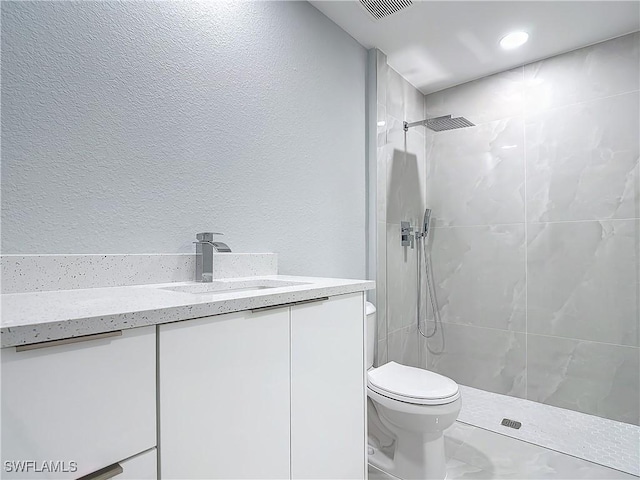 bathroom with toilet, tiled shower, and vanity