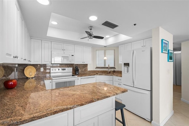 kitchen with a raised ceiling, white cabinetry, white appliances, and kitchen peninsula