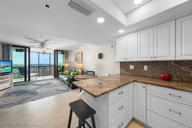 kitchen featuring floor to ceiling windows, tasteful backsplash, kitchen peninsula, white cabinets, and dark stone counters