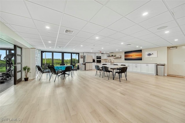 dining space featuring a paneled ceiling, a wall of windows, and light wood-type flooring