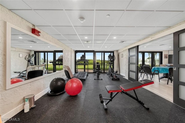 gym with french doors, expansive windows, and a drop ceiling