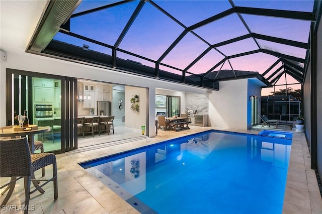 pool at dusk with glass enclosure and a patio