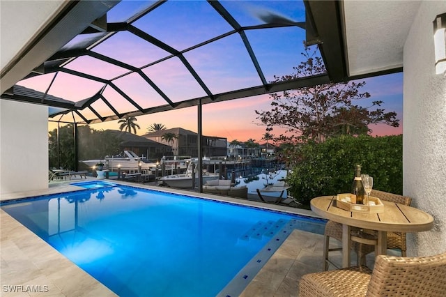 pool at dusk featuring a boat dock, a patio area, and glass enclosure