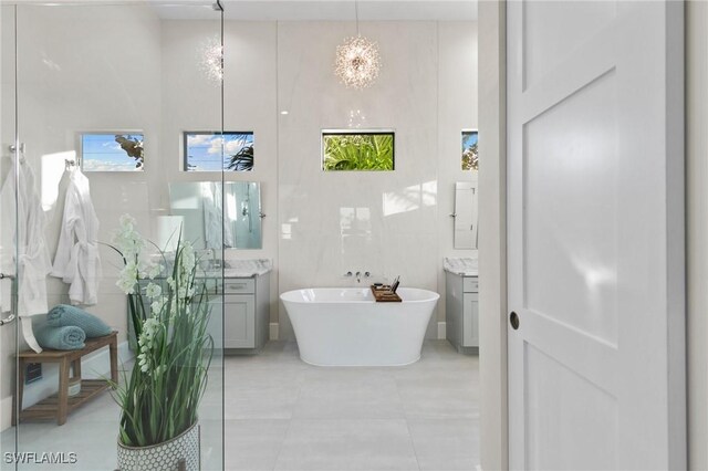 bathroom featuring tile patterned floors, vanity, an inviting chandelier, tile walls, and a bathtub