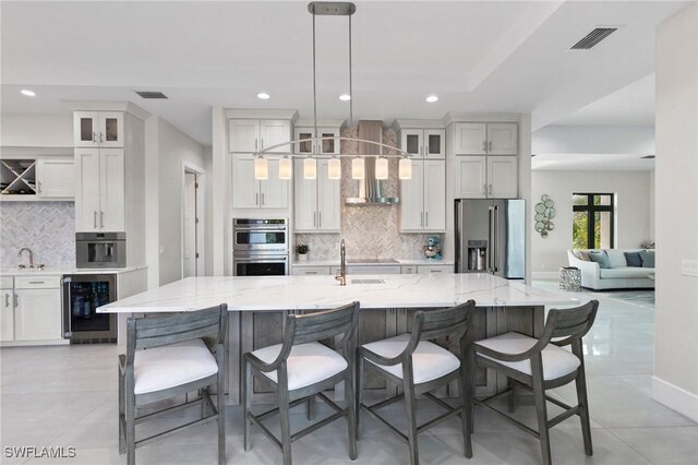 kitchen featuring a large island with sink, beverage cooler, stainless steel appliances, backsplash, and hanging light fixtures