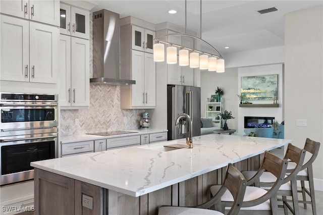 100 Templewood Ct, Marco Island, FL 34145 - kitchen with wall chimney exhaust hood, appliances with stainless steel finishes, an island with sink, decorative backsplash, and a breakfast bar area