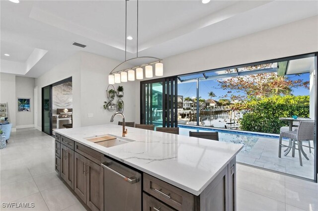 kitchen featuring decorative light fixtures, dishwasher, a raised ceiling, sink, and light stone counters