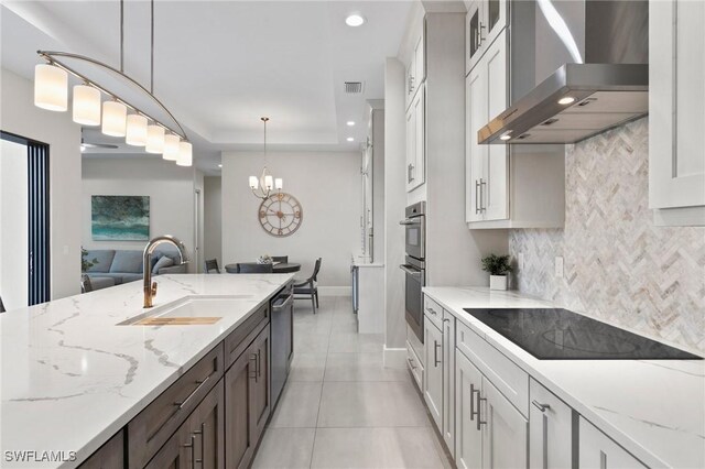 kitchen featuring appliances with stainless steel finishes, white cabinets, decorative light fixtures, wall chimney range hood, and sink