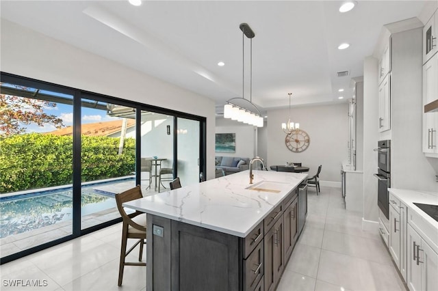 kitchen featuring an island with sink, white cabinets, decorative light fixtures, and sink