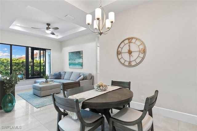 tiled dining room featuring ceiling fan with notable chandelier and a tray ceiling