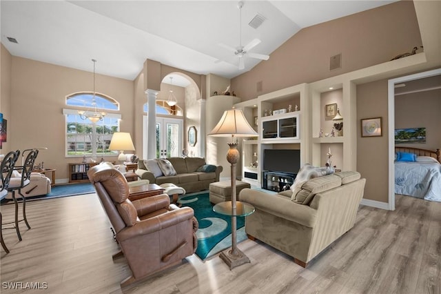 living room with light hardwood / wood-style flooring, high vaulted ceiling, built in shelves, ceiling fan with notable chandelier, and ornate columns