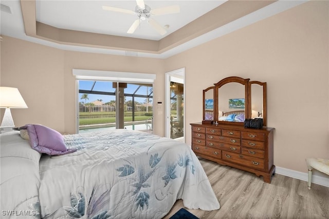 bedroom featuring light wood-type flooring, ceiling fan, a raised ceiling, and access to outside