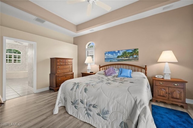 bedroom featuring ceiling fan, connected bathroom, hardwood / wood-style flooring, and a tray ceiling