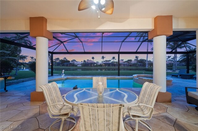 pool at dusk featuring glass enclosure, an in ground hot tub, ceiling fan, and a patio