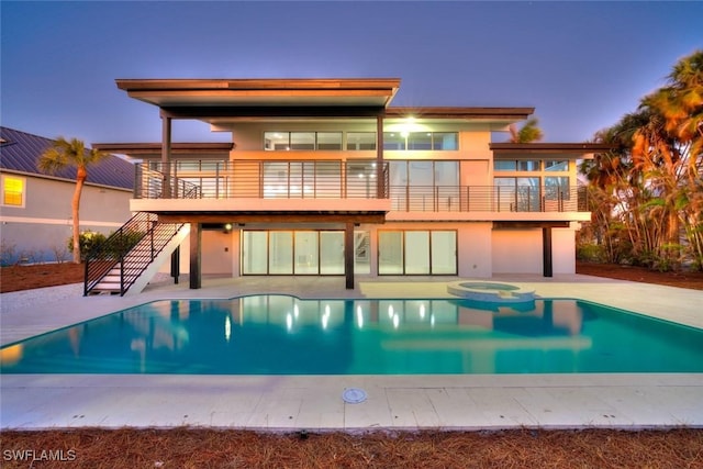 back house at dusk featuring a swimming pool with hot tub and a patio area