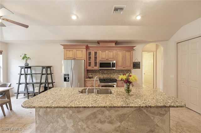 kitchen with a center island with sink, stainless steel appliances, decorative backsplash, light stone countertops, and sink