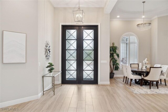 foyer entrance featuring light wood-type flooring, french doors, a notable chandelier, and ornamental molding