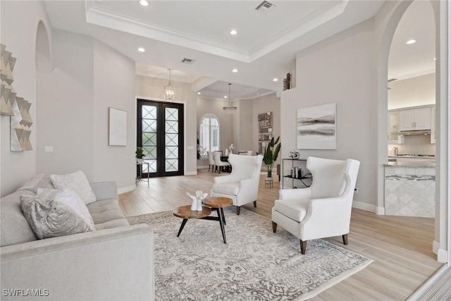 living room with french doors, a notable chandelier, a tray ceiling, and light hardwood / wood-style flooring