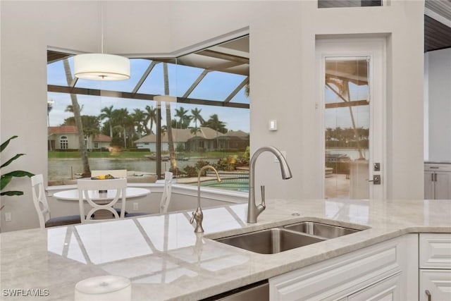 kitchen with light stone countertops, white cabinetry, a water view, and sink