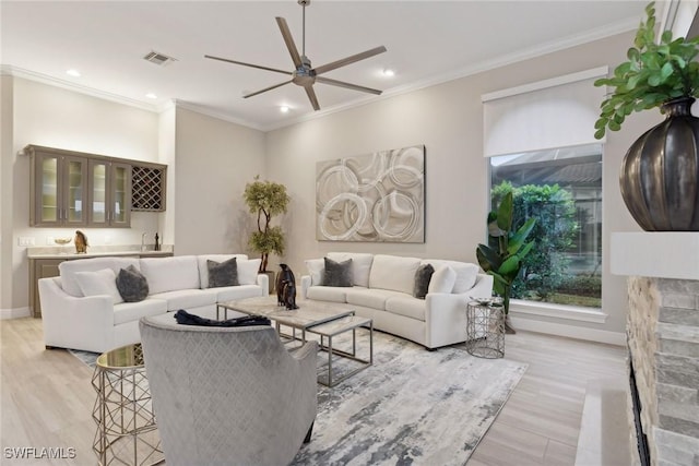 living room featuring ceiling fan, ornamental molding, indoor bar, and light wood-type flooring