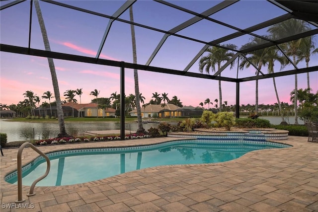 pool at dusk with glass enclosure, a patio area, and a water view