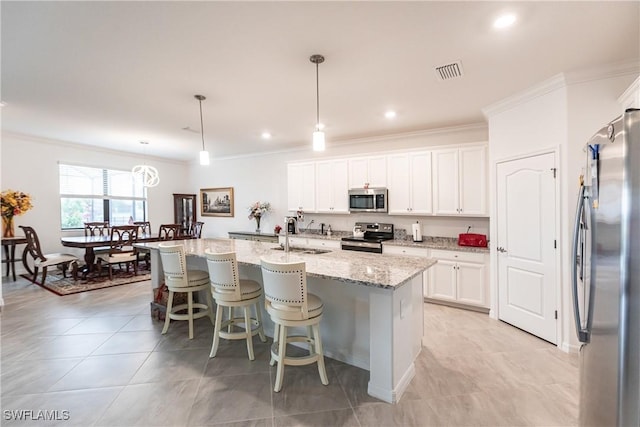 kitchen featuring white cabinetry, an island with sink, stainless steel appliances, decorative light fixtures, and light stone counters