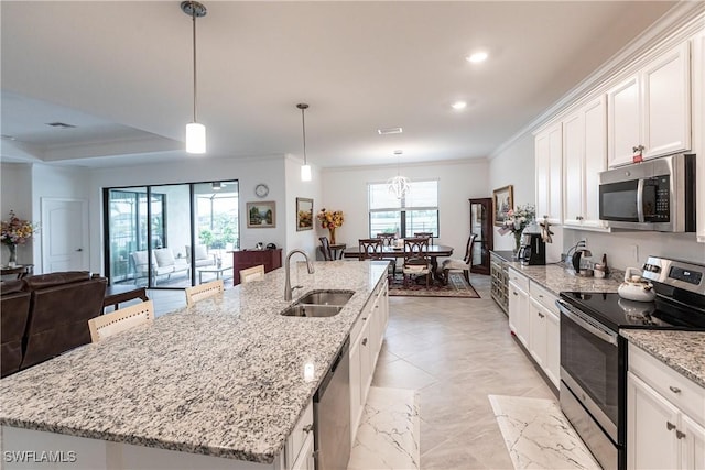 kitchen featuring white cabinetry, an island with sink, appliances with stainless steel finishes, decorative light fixtures, and sink